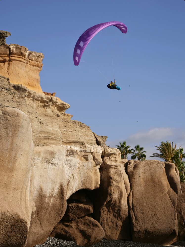 A paraglider flying beside a dramatic cliff